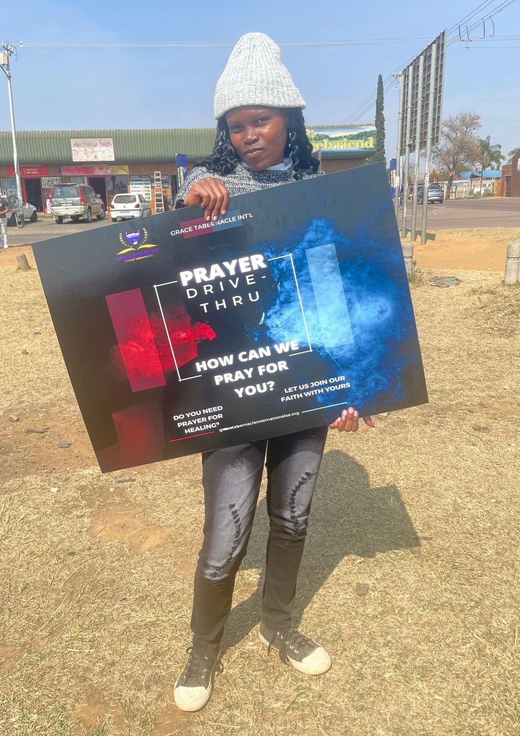 Person holding a Prayer Drive-Thru sign outdoors on a sunny day.